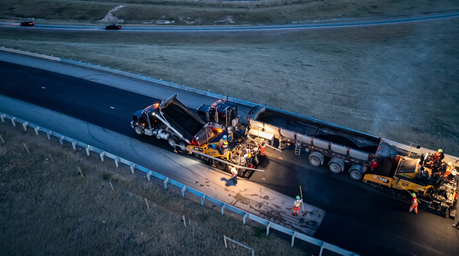 Aerial night photograph of highway paving, A.F. Trucking dump truck tipping asphalt into the paver